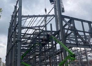 An image of a steel frame in construction with two green cranes